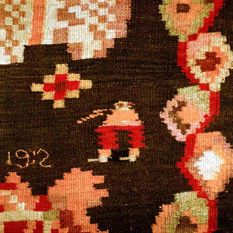 Detalle de una alfombra moldava tejida a mano con motivos florales y geométricos en rojo, crema y verde sobre un fondo oscuro
